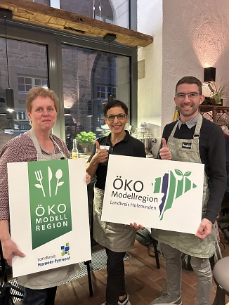 Auf dem Bild sehen Sie drei Personen die zwei Schilder in der Hand halten. Schilderbeschriftung lautet: Ökomodellregion Landkreis Hameln-Pyrmont und Ökomodellregion Landkreis Holzminden.&nbsp;&copy;&nbsp;Landkreis Holzminden