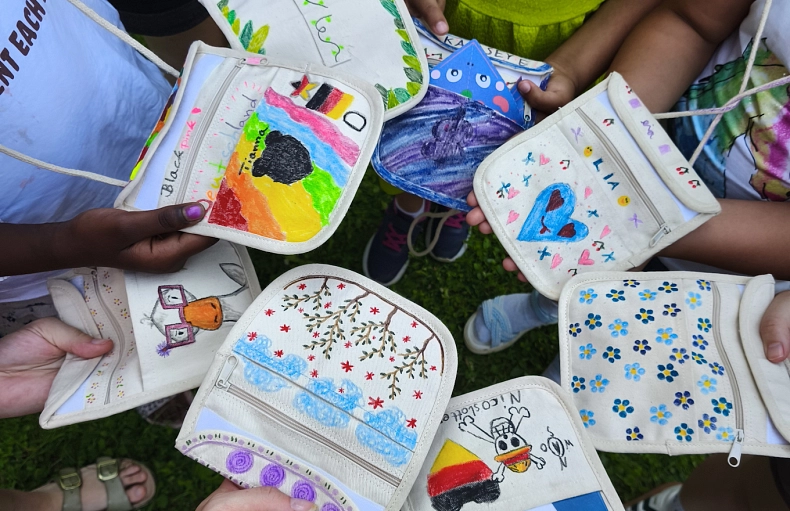 2026-07-22 PM Balu und du Kinder stehen im Kreis und halten selbstgebastelte und bunte Umhängetäschchen in die Kamera.