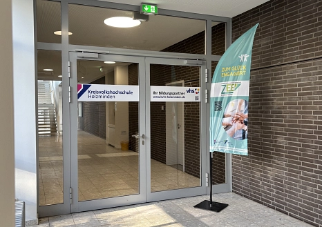 Eine Glastür in einem Gang mit der Beschriftung "Kreisvolkshochschule Holzminden". daneben ein Aufsteller mit der Beschriftung "Zentrum für ehrenamtliches Engagement ZEE im Landkreis Holzminden"