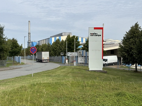 Eine Straße mit einem LKW vor einem Fabrikgelände, davor ein Schild mit der Aufschrift "noelle + von campe"